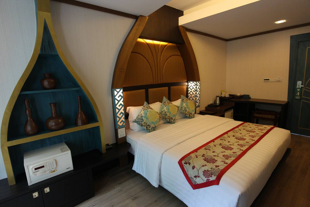A neatly arranged hotel room with a bed, a decorative shelf with vases, and a small desk with a telephone.