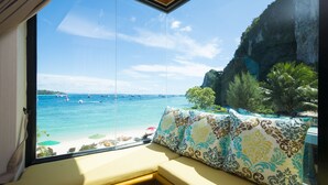 A room with a large window overlooking a beach, a cushioned bench, and a patterned pillow. - Phi Phi Nice Beach Hotel Hip (Ko Phi Phi)