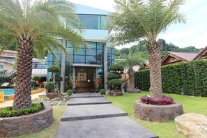 A modern building with a glass facade, a stone pathway leading to the entrance, and well-maintained landscaping including palm trees and shrubs. - Phi Phi Nice Beach Hotel Hip (Ko Phi Phi)