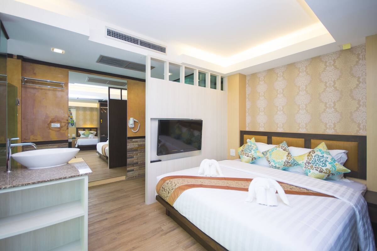 A modern hotel room with a large bed, a TV, a bathroom with a sink and mirror, and a view of the city.