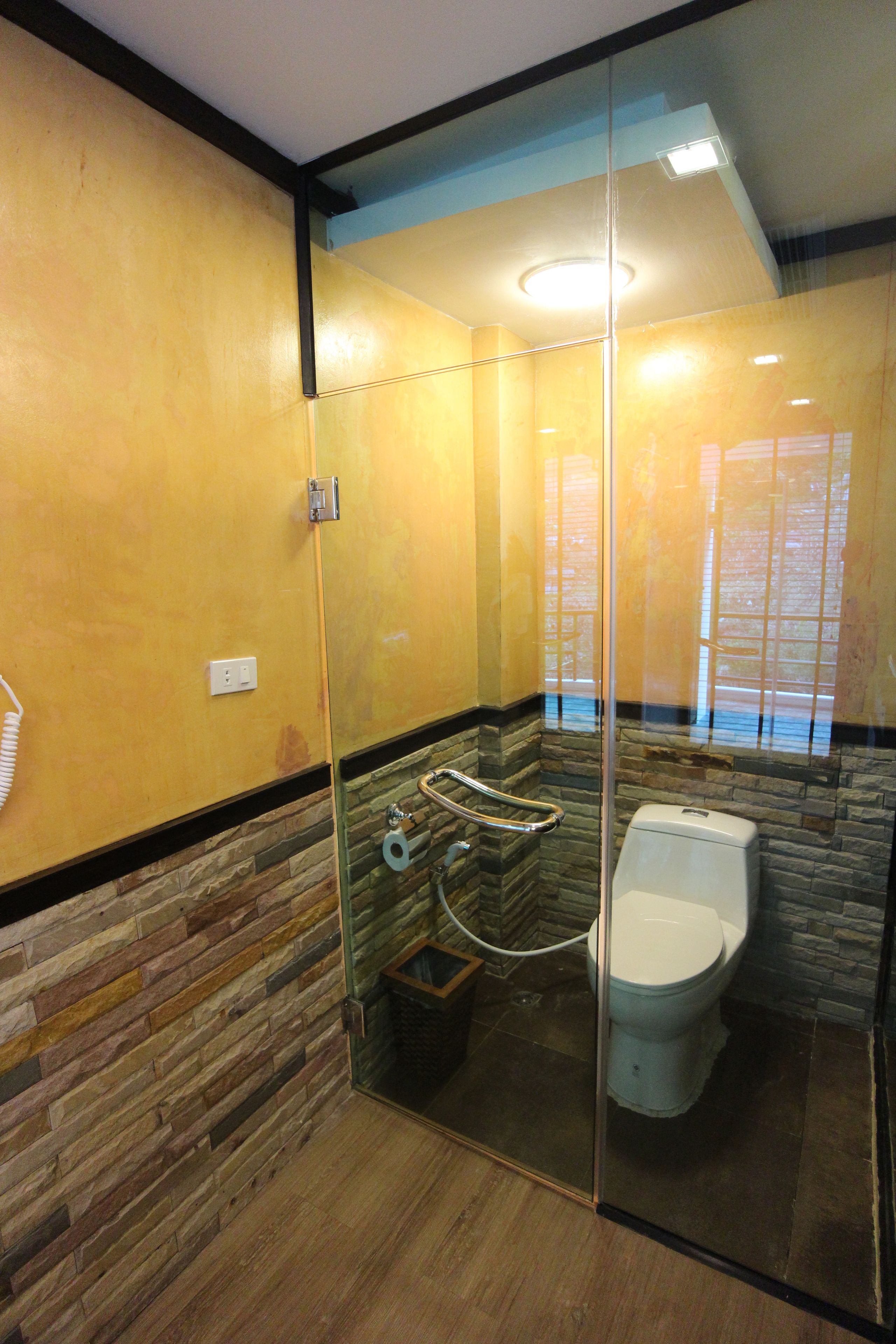 Un baño moderno con ducha envuelta en vidrio, inodoro y pared con diseño de piedra.