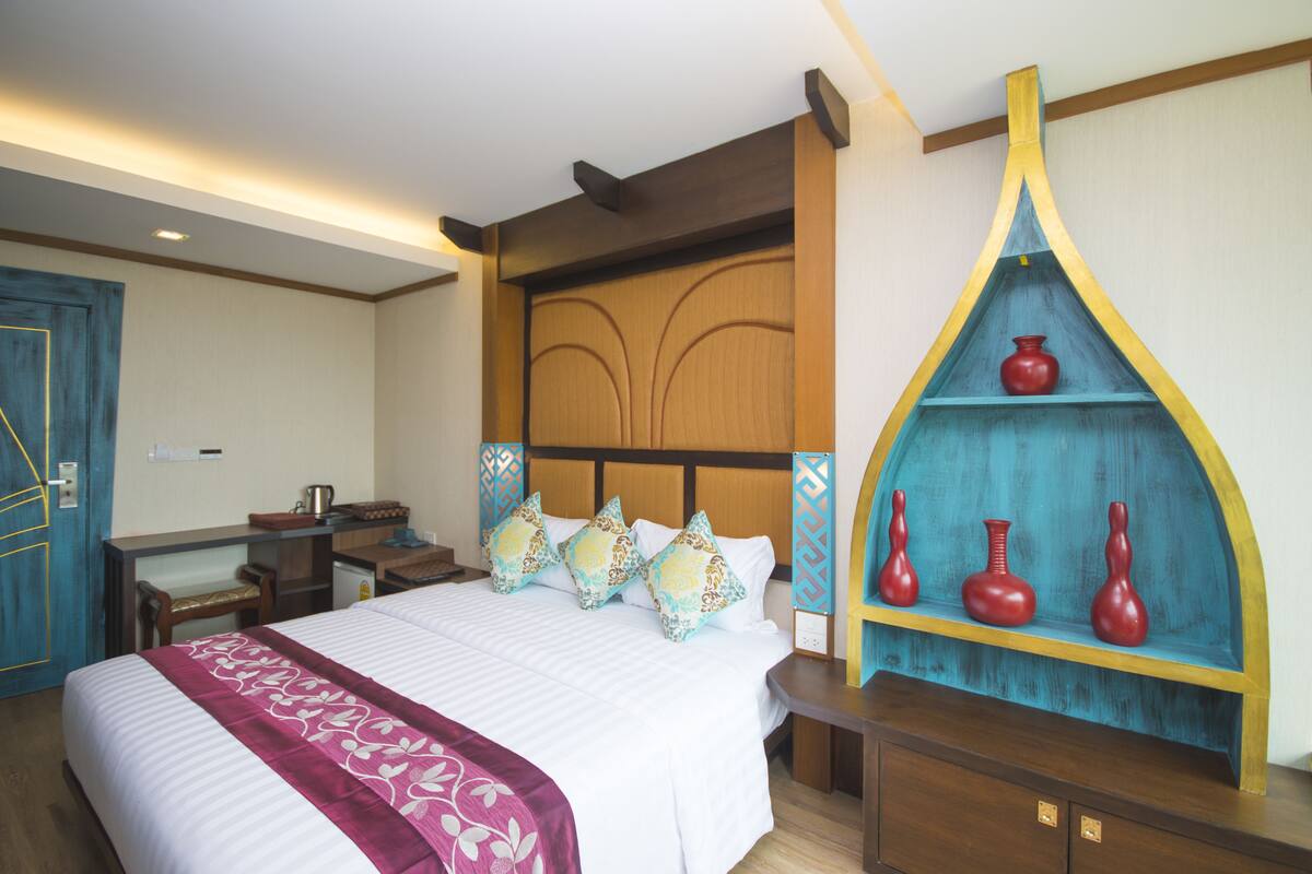 A hotel room with a large bed, a wooden headboard, a desk with a chair, and a decorative shelf with vases.