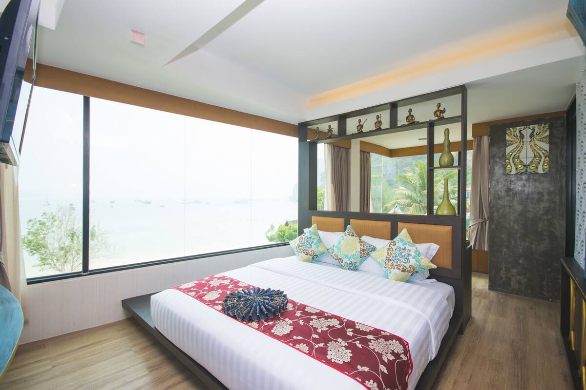 A modern hotel room with a large bed, a view of the sea, and a balcony with a view of palm trees.