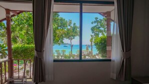 Un dormitorio con un ventanal grande, una cama y vistas al mar y a los árboles.