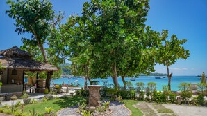 Un resort tropical con una cabaña de techo de paja, un pozo de piedra y vistas al mar con barcos.