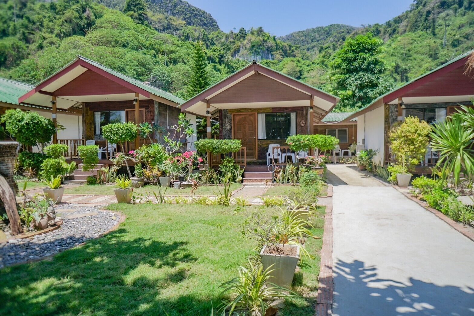 A row of three wooden cabins with a garden in front, surrounded by lush greenery and hills.
