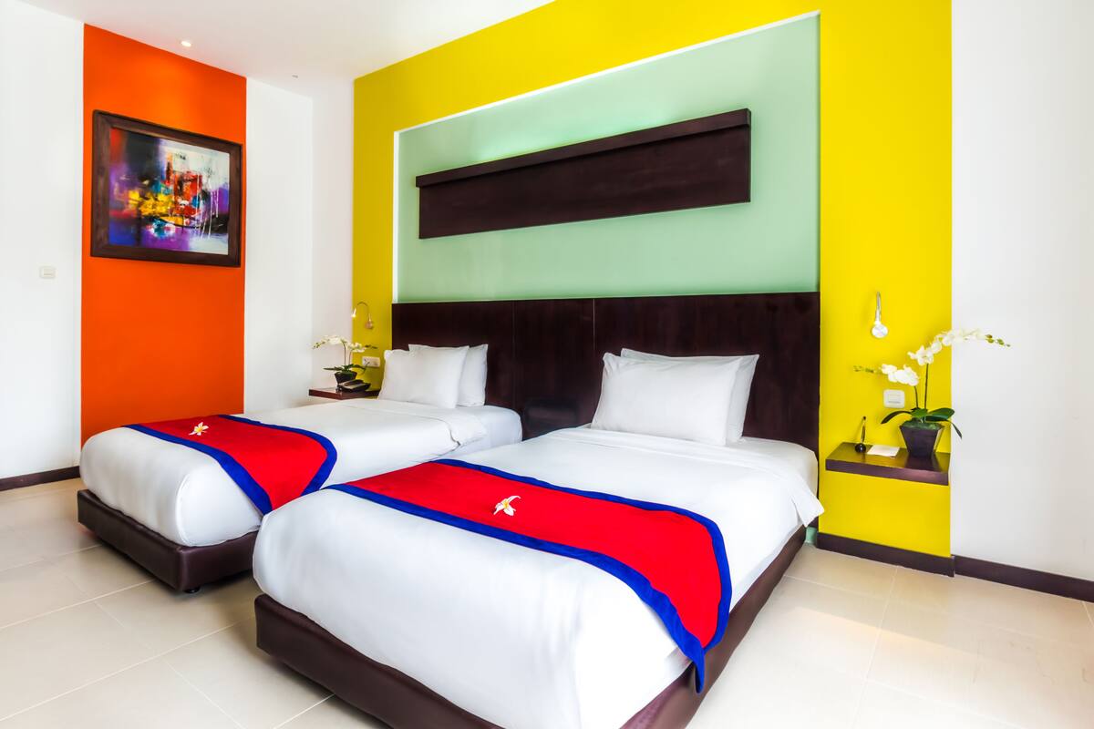 Une chambre d’hôtel avec deux lits, une grande peinture abstraite et un mur d’accent d’un jaune vif.