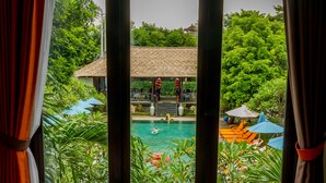 A view of a swimming pool with a thatched-roof structure in the background, surrounded by lush greenery. - Ozz Hotel - Kuta Bali (Kuta)