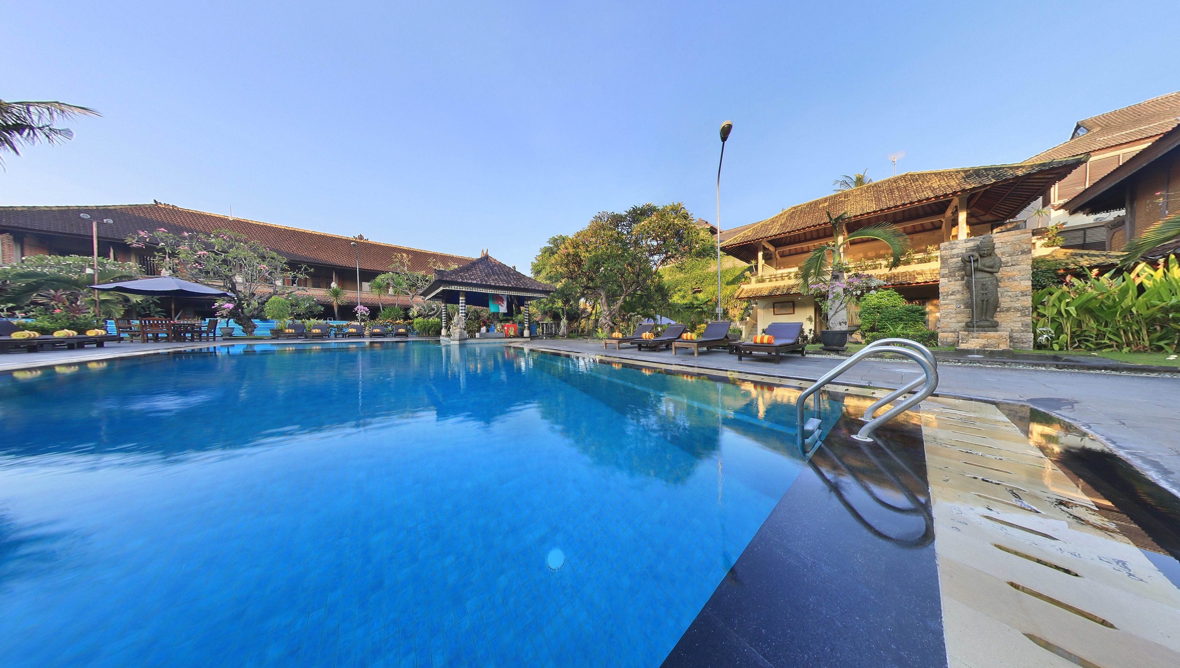 A swimming pool with lounge chairs and umbrellas, surrounded by buildings with tiled roofs and greenery.