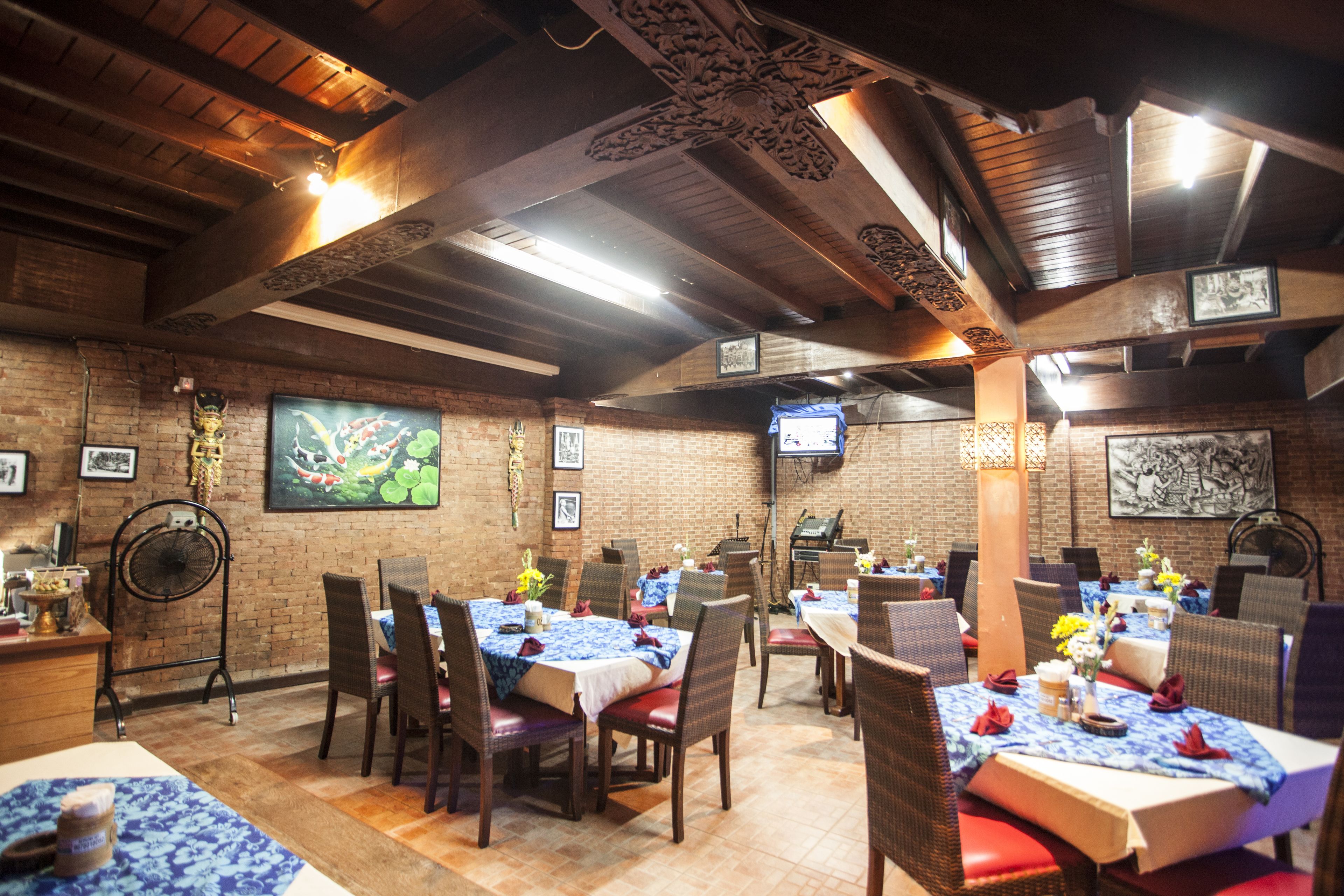 A restaurant with brick walls, wooden beams, and tables set with blue tablecloths and red chairs.