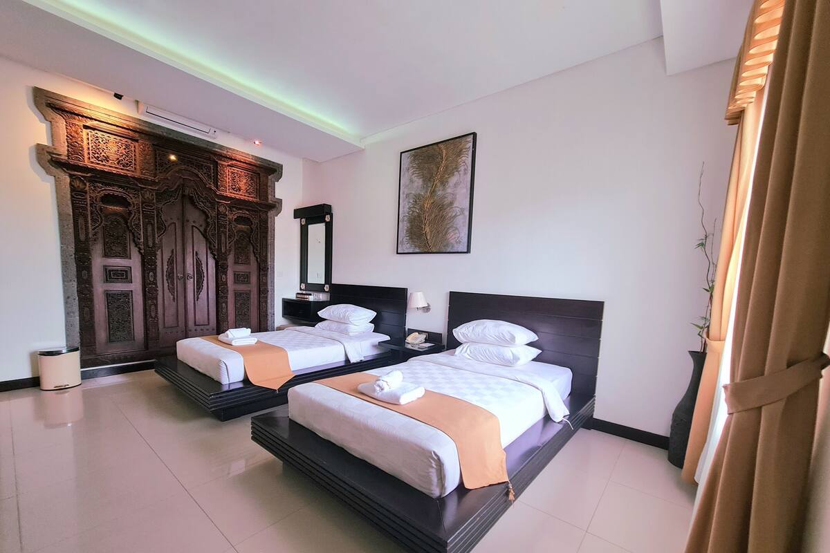 Habitación de hotel con dos camas, un espejo grande, un cuadro y una puerta decorativa.