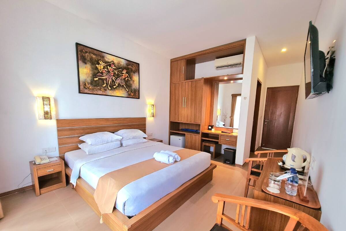 Habitación de hotel con una cama grande, un escritorio con una silla, una pequeña cocina y un espejo, además de un cuadro en la pared.