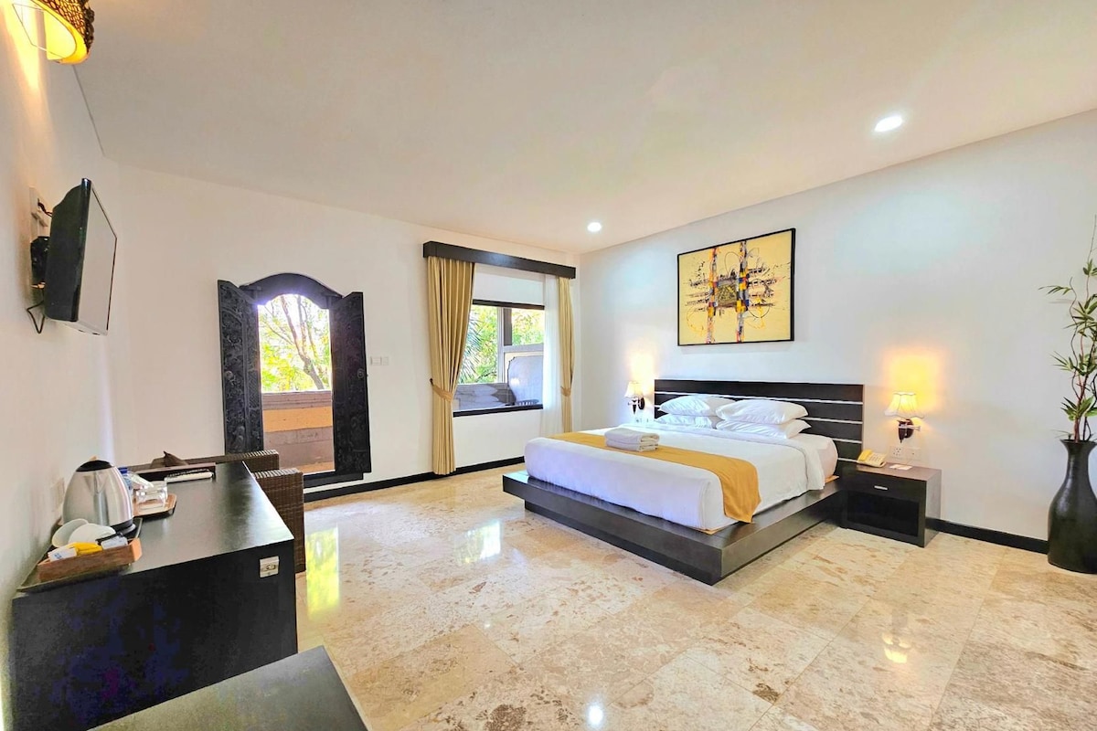 A hotel room with a bed, bedside tables, a desk, a television, and a window with curtains.