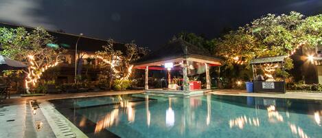 A nighttime swimming pool area with a covered seating area and string lights.