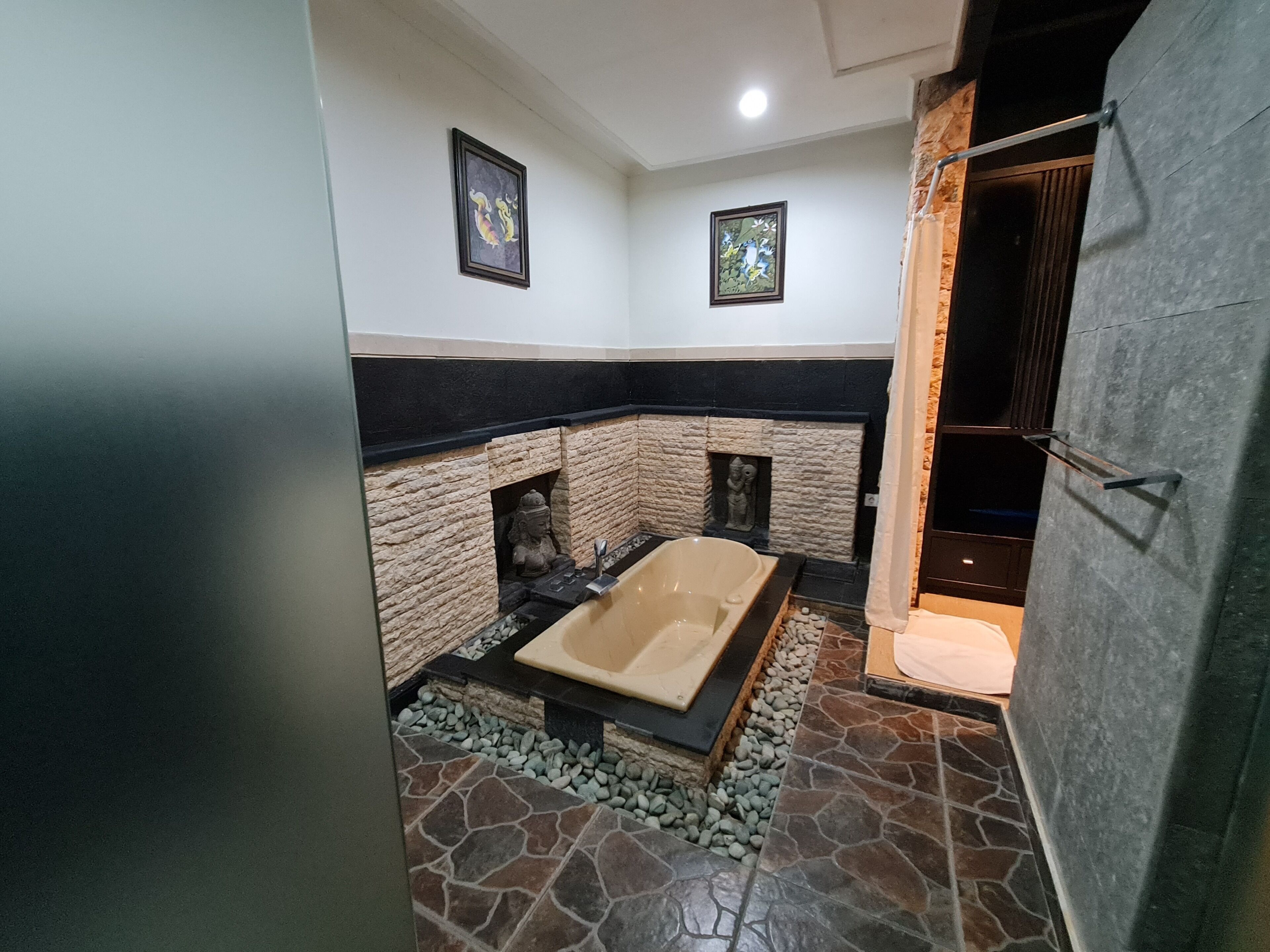 A bathroom with a stone floor, a bathtub, and a shower area.