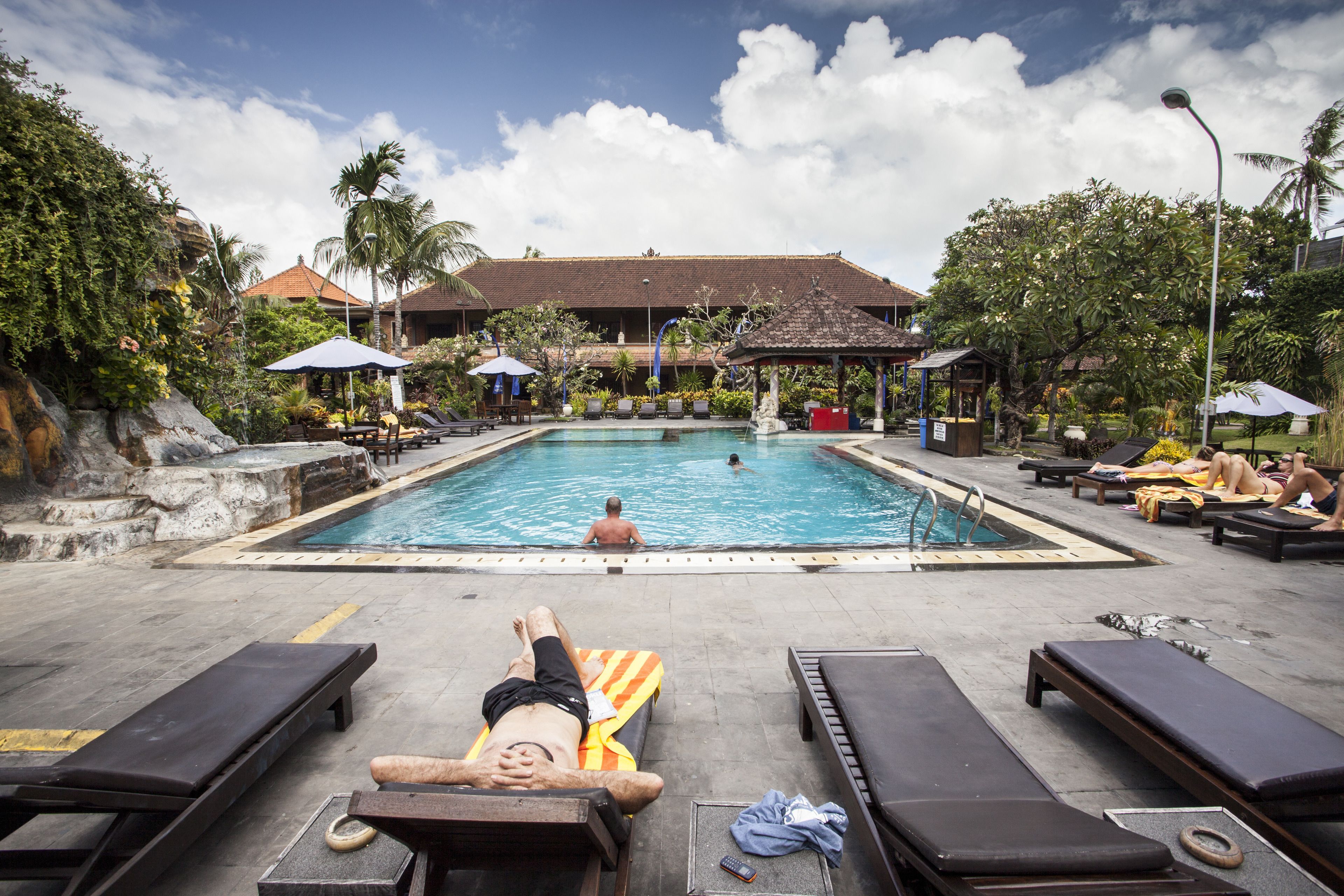 A pool area with lounge chairs, umbrellas, and a building in the background.