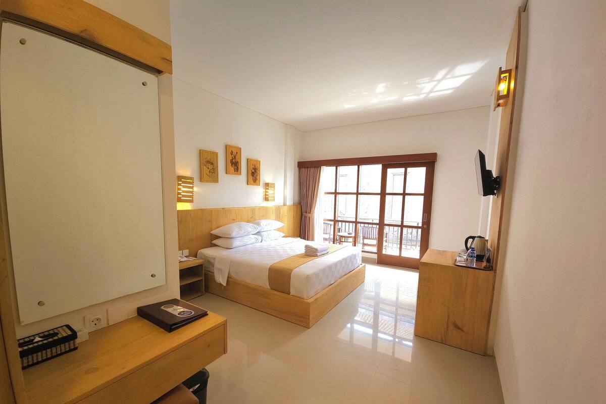 Una habitación de hotel con cama, mesita de noche, escritorio y un amplio ventanal.