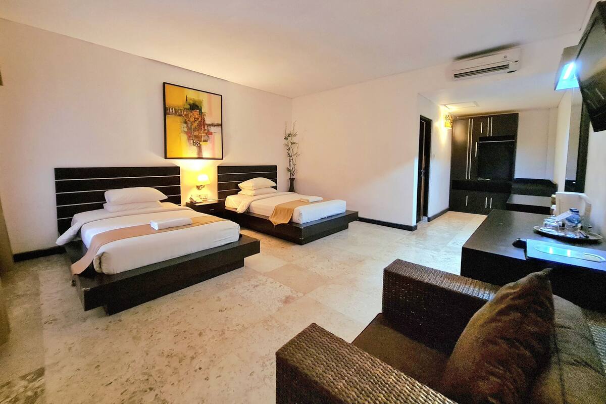 Habitación de hotel con dos camas, una mesa de comedor, un sofá y un televisor.