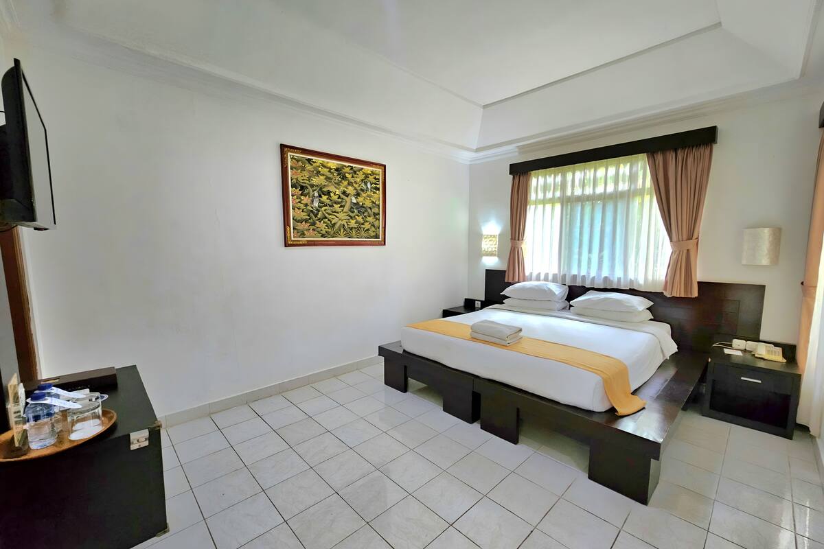 Una habitación de hotel con cama, mesitas de noche, un escritorio con teléfono y un cuadro en la pared.