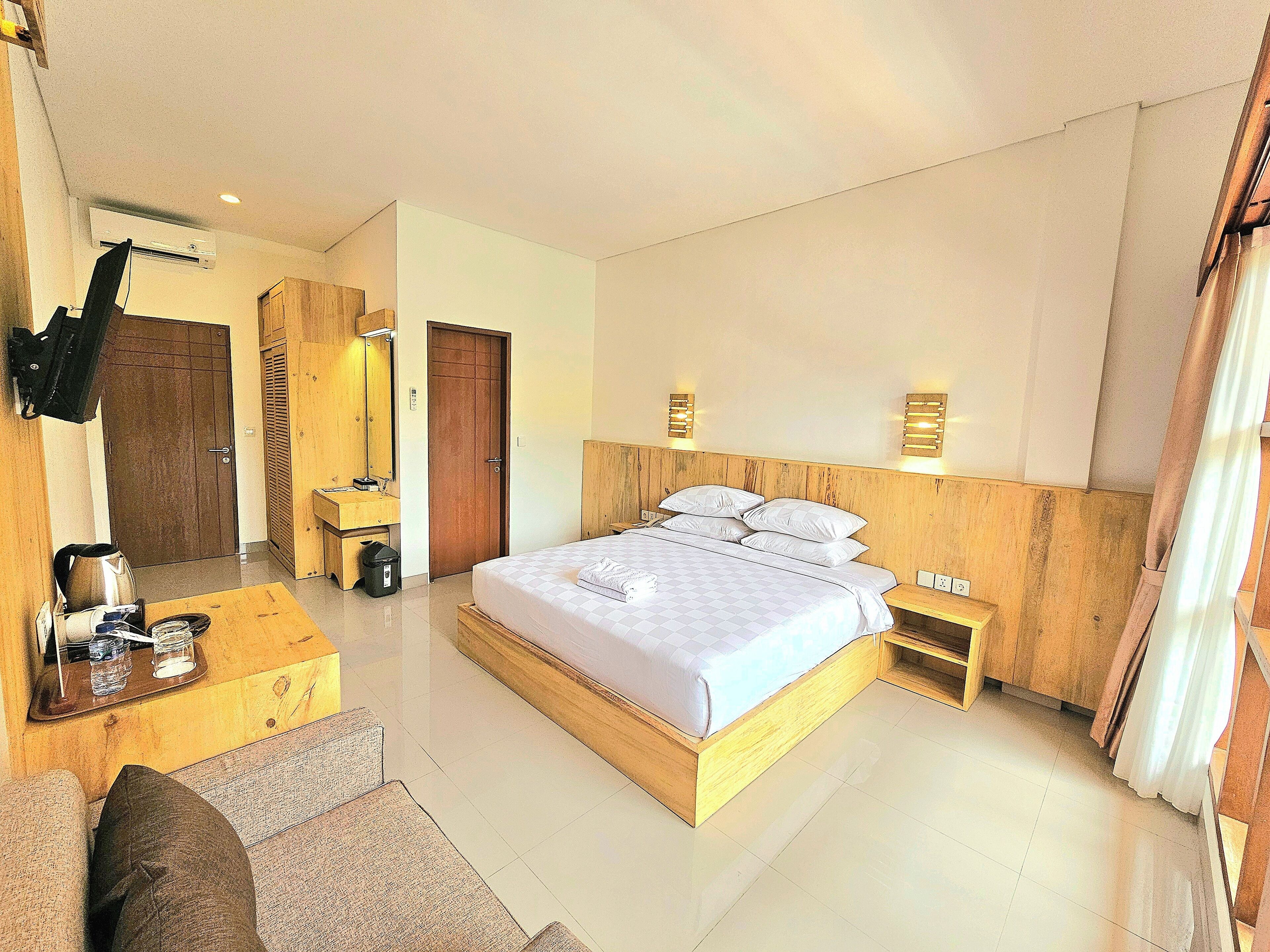 A hotel room with a large bed, a wooden headboard, a desk with a chair, a small table, and a wardrobe.