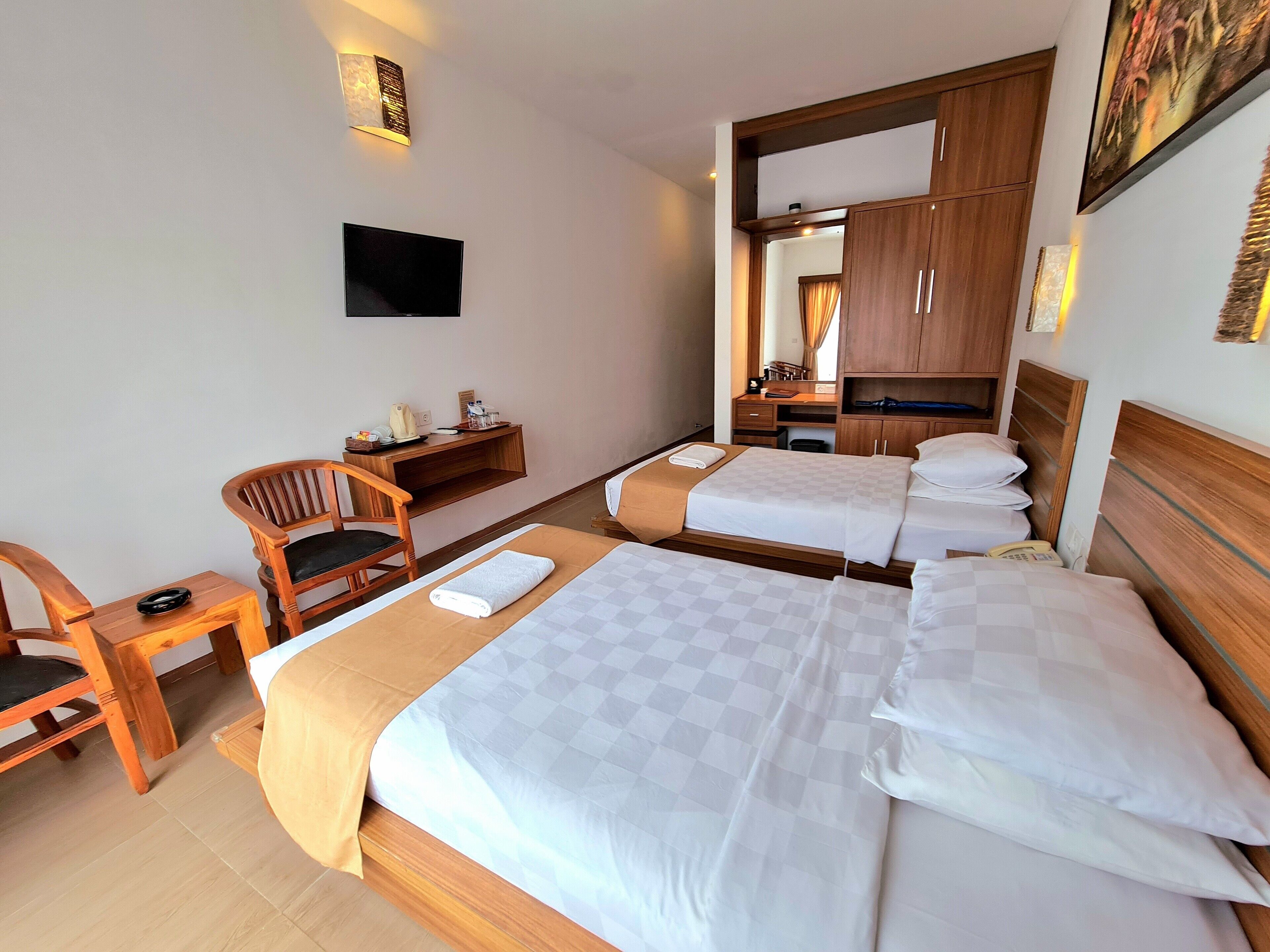 A hotel room with two beds, a desk, a chair, a flat-screen TV, and a mirror.