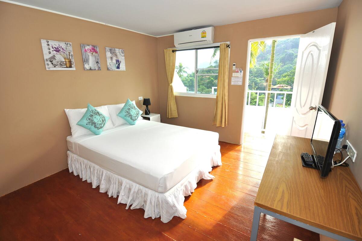 A bedroom with a bed, a desk with a computer, a window with curtains, and wall art.