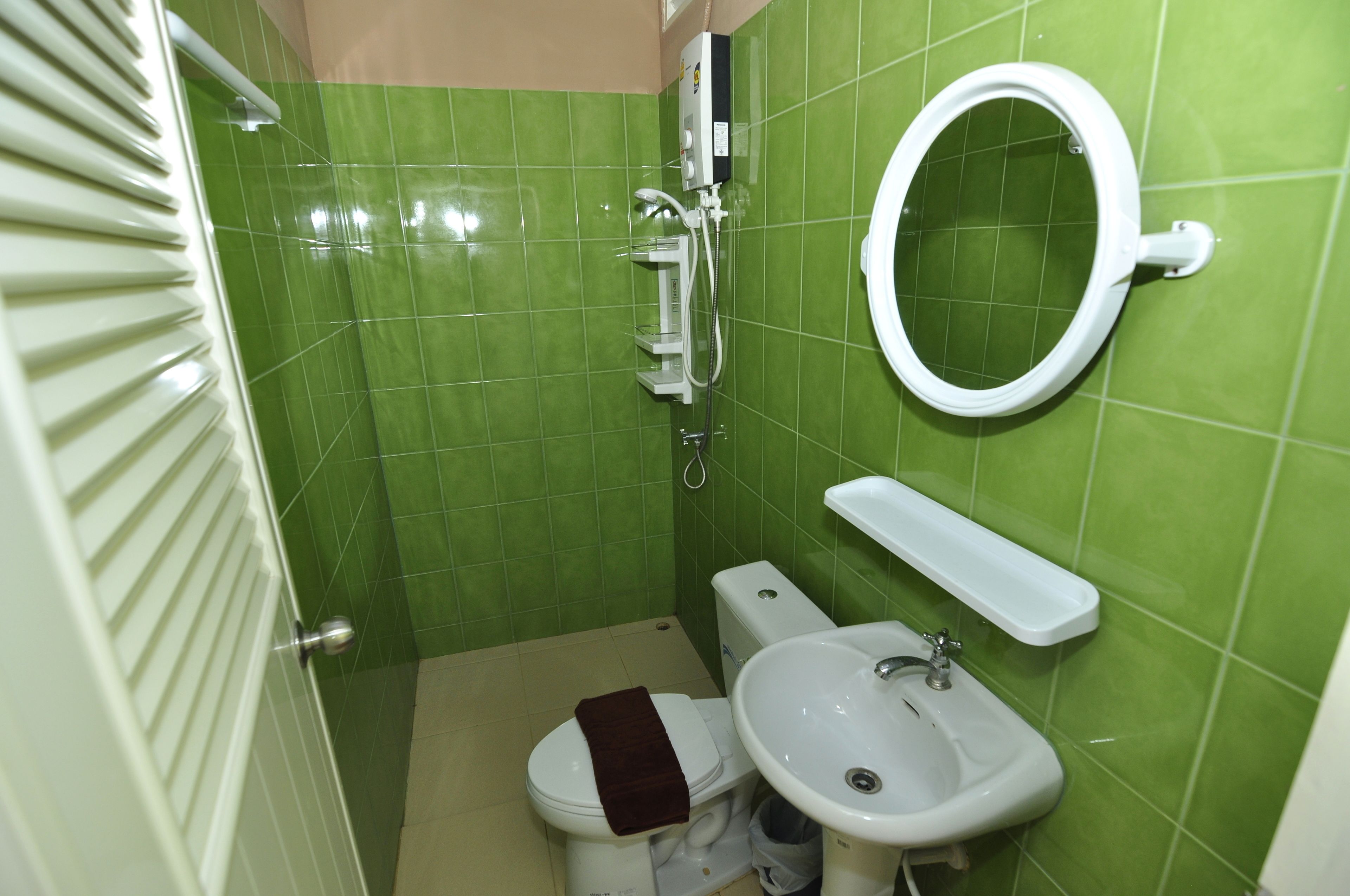 A small bathroom with green tiles, a toilet, a sink, and a mirror.