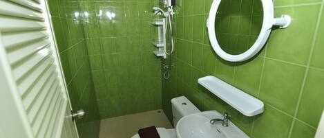 A small bathroom with green tiles, a toilet, a sink, and a mirror.