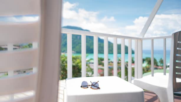 A balcony with a white railing, a small table, and a pair of sunglasses on the table.