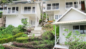 A residential building with multiple balconies, a staircase leading to the upper floors, and a well-maintained garden with various plants and flowers.