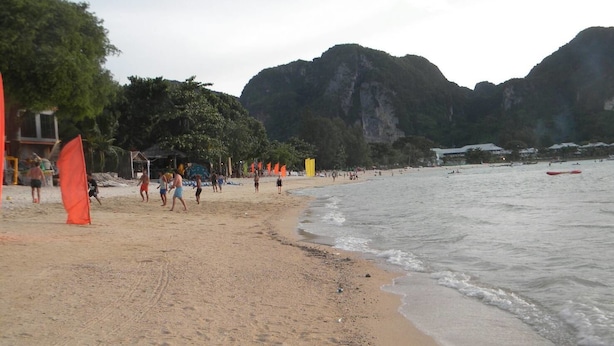 Una playa con gente caminando, una orilla arenosa y montañas al fondo.