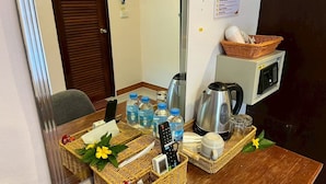 Una mesa ordenada con una tetera, botellas de agua, un control remoto y una cesta con flores.