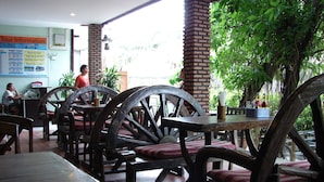 Un restaurante con mobiliario de madera, incluyendo sillas con ruedas grandes y mesas. Hay un cartel con información en la pared, y se ve a una persona al fondo.