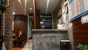 Un área de recepción con un letrero de 'SABAI HOUSE', un pilar de madera, un espacio para sentarse y una pared con un panel de menú.