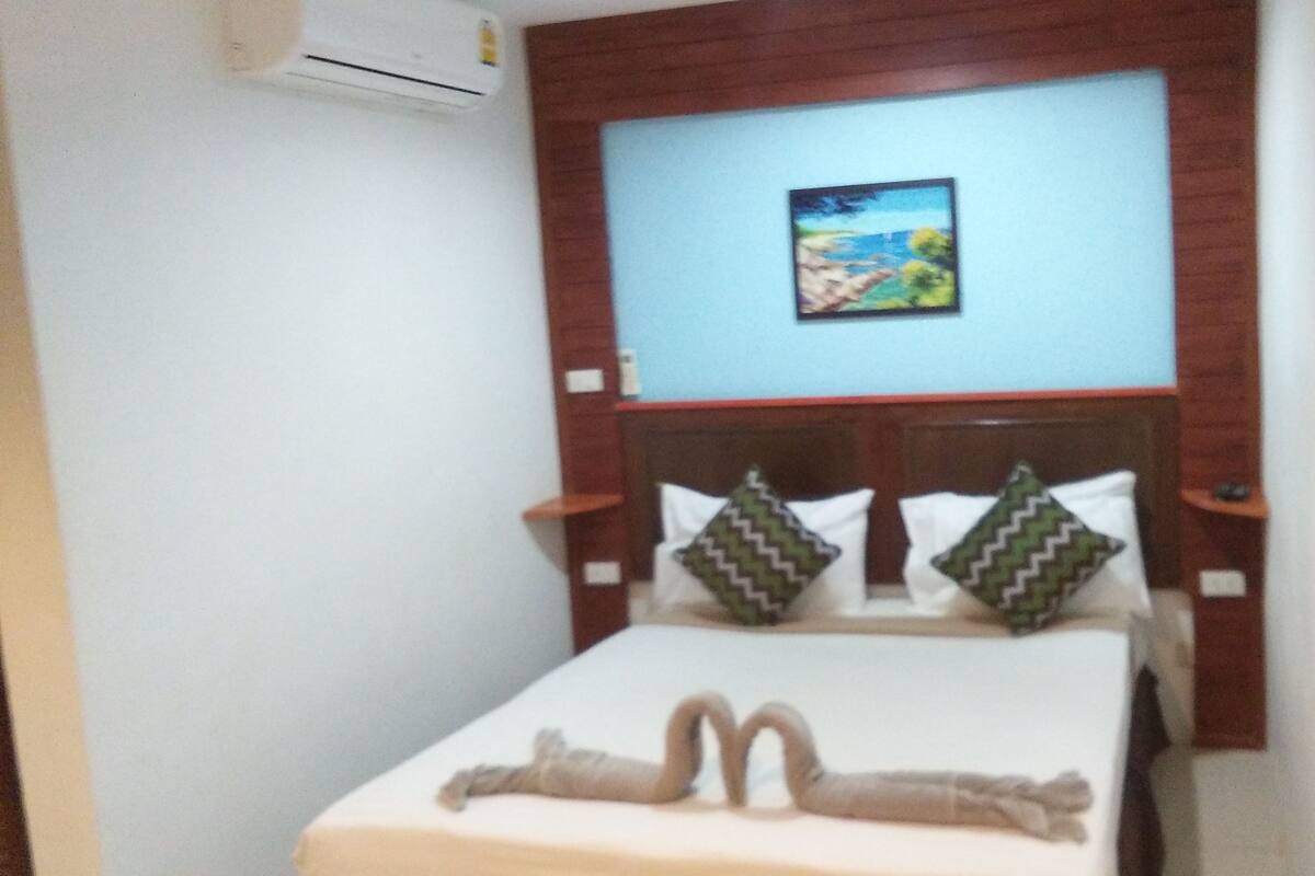 A hotel room with a bed, a headboard, and a wall-mounted air conditioner.