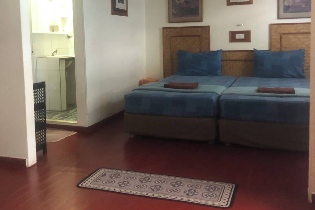 A bedroom with two beds, a small desk, and a bathroom visible through an open door.