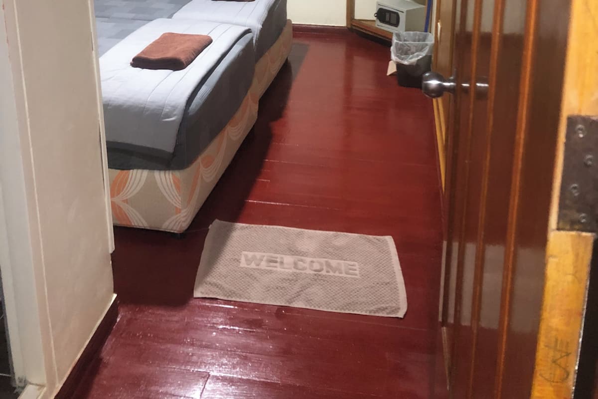 A narrow hallway leading to a bedroom with two beds, a small shelf with toiletries, and a welcome mat.