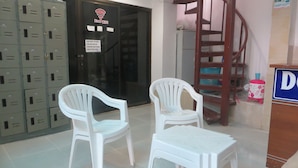A room with two white plastic chairs, a small table, a staircase, and a row of grey lockers. - Lucky House Dorm Room - Hostel (Ko Phi Phi)