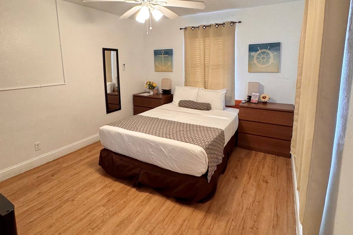 Une chambre à coucher avec un lit, une table de chevet, un ventilateur de plafond et une fenêtre avec des rideaux.