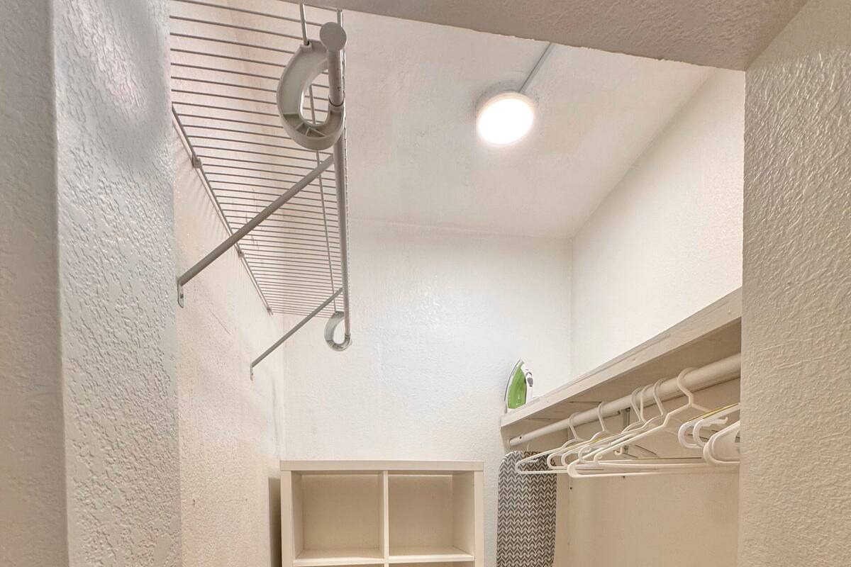 Un petit placard bien éclairé, doté d’étagères et d’une tringle pour suspendre les vêtements, d’un portant métallique et d’un sol carrelé.
