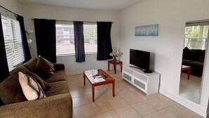 A living room with a sofa, coffee table, TV, and windows with curtains. - Coral Key Inn (Lauderdale-by-the-Sea)