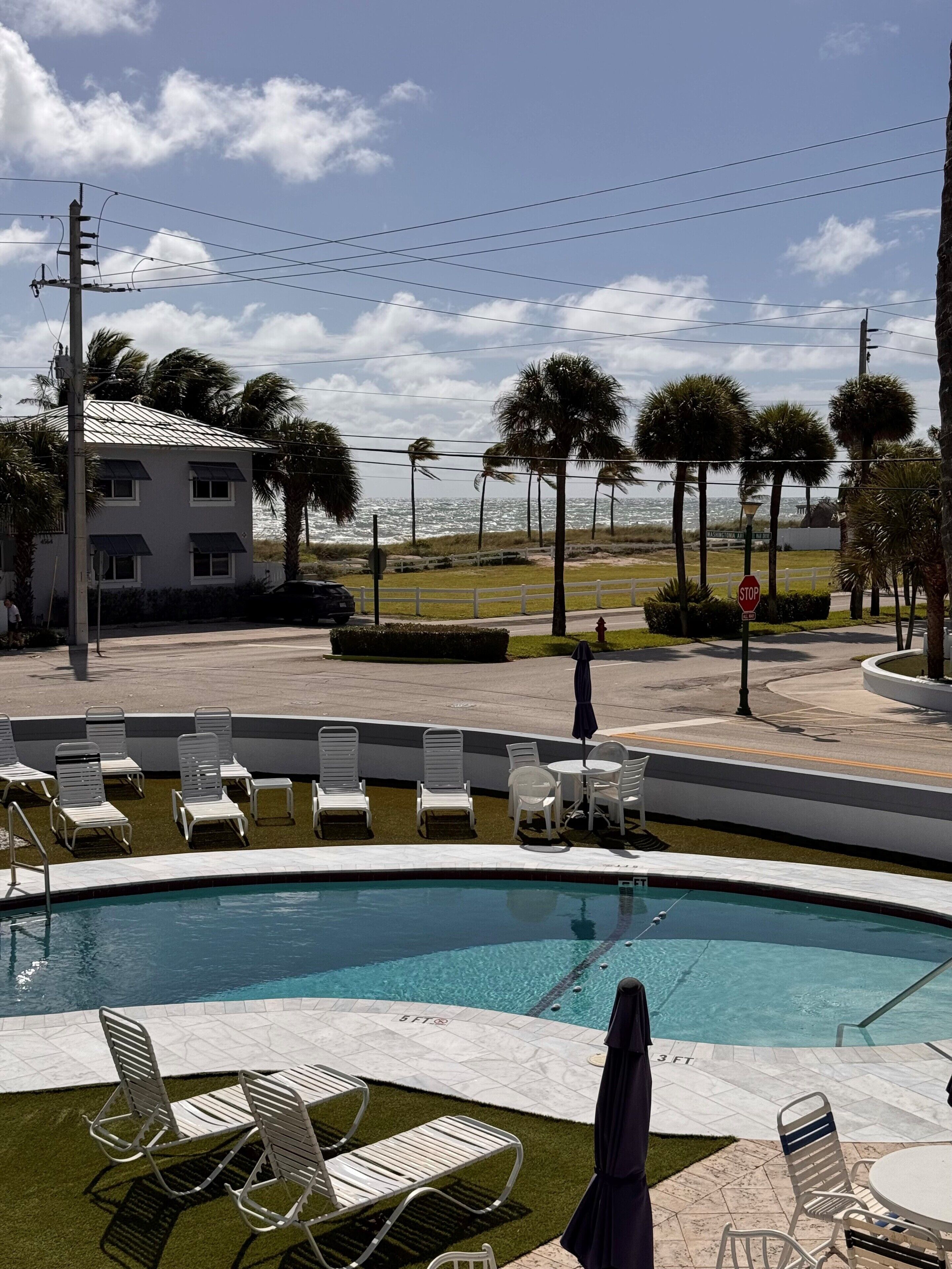 A pool area with lounge chairs and a view of the ocean.