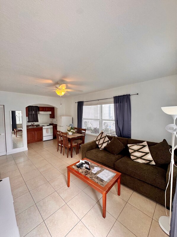 A living room with a sofa, coffee table, and a dining area with chairs and a table.