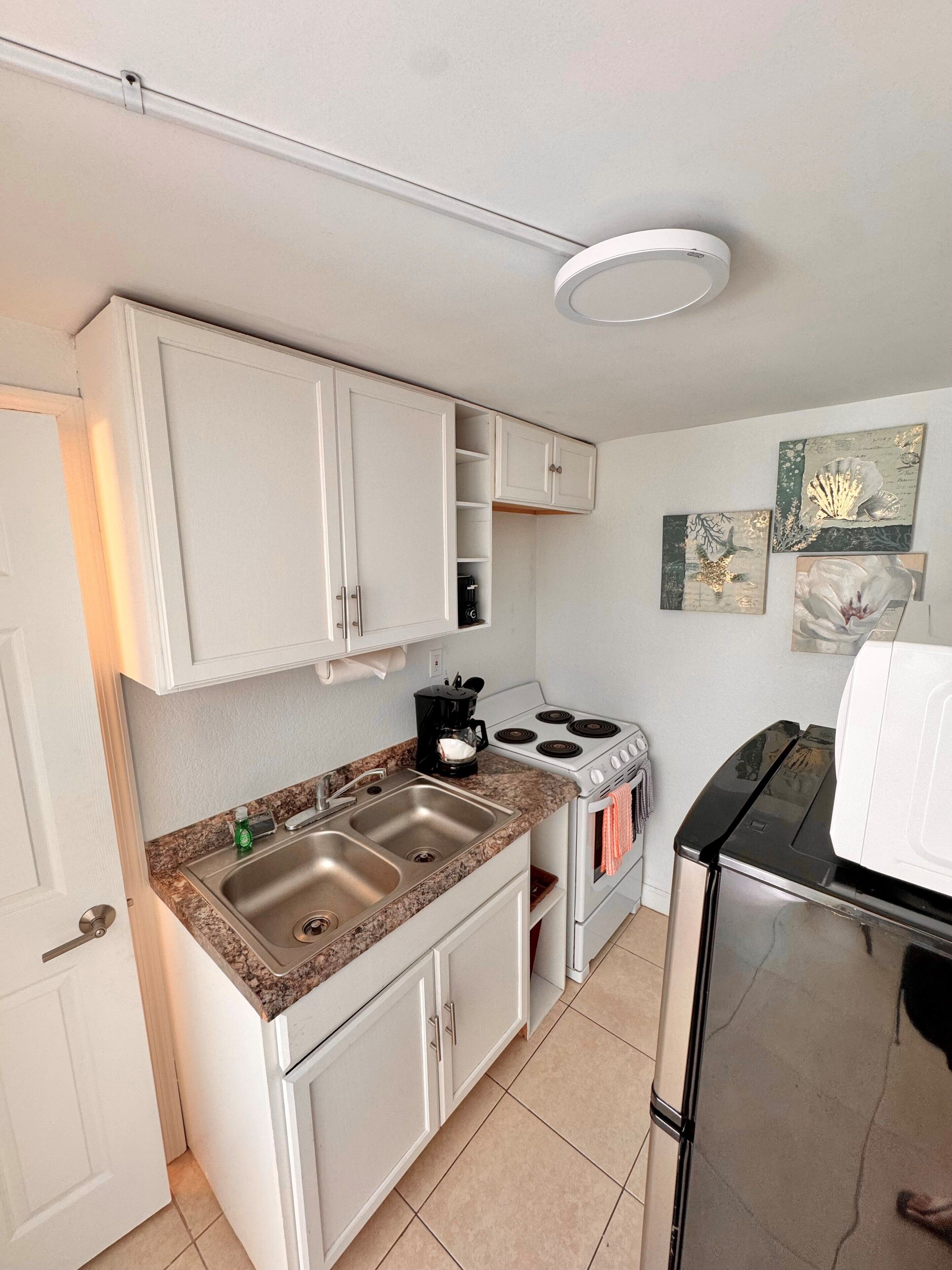 A compact kitchen with white cabinets, a double sink, a stove, and a microwave.