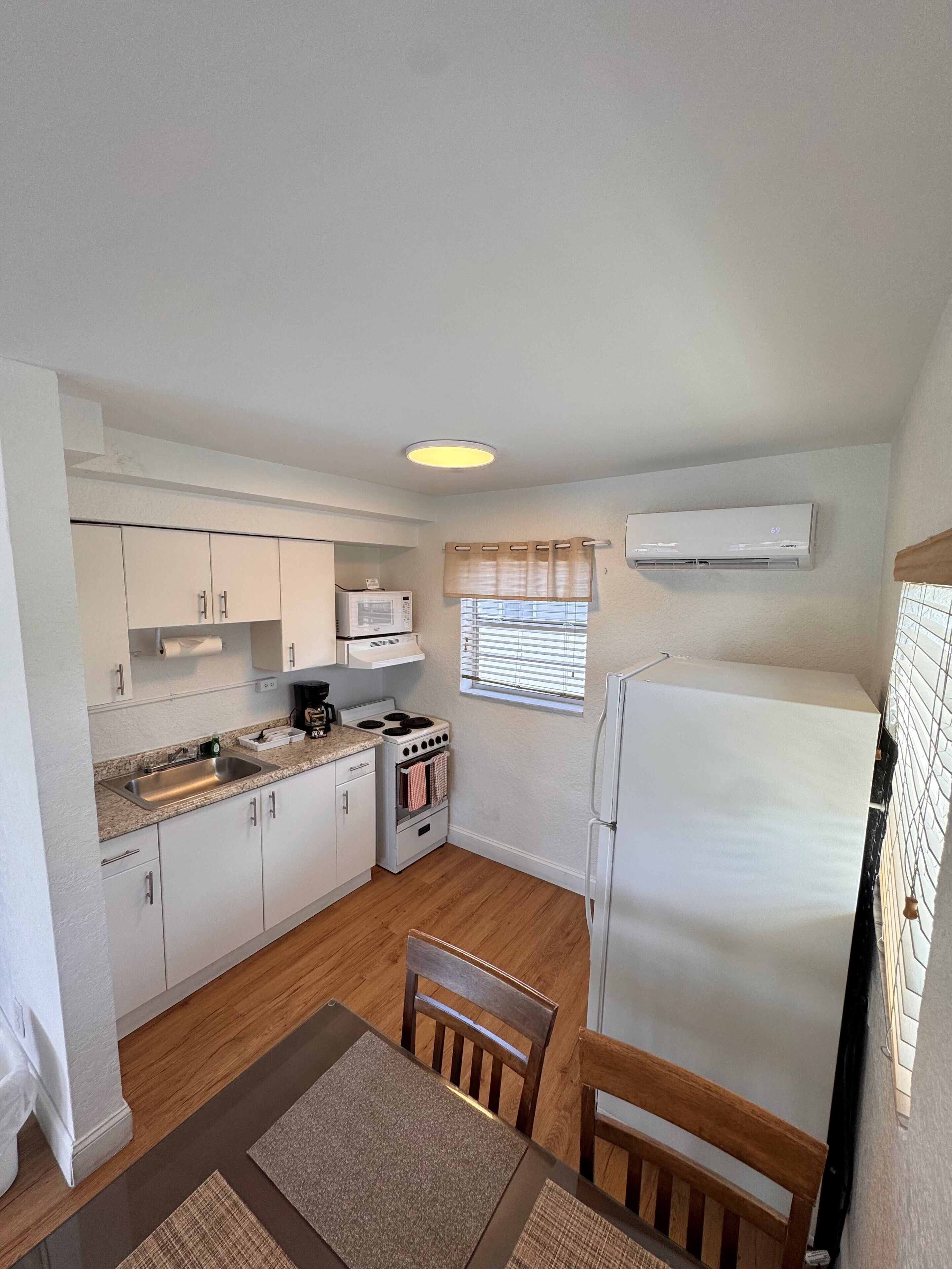 A compact kitchen with white cabinets, a microwave, stove, and a refrigerator.