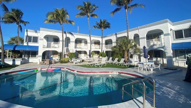 A pool area with lounge chairs and palm trees, surrounded by a building with balconies. - Coral Key Inn (Lauderdale-by-the-Sea)