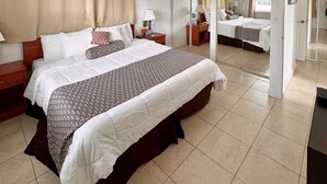 A hotel room with a large bed, a bedside table with a lamp, a wardrobe, and a mirror. - Coral Key Inn (Lauderdale-by-the-Sea)