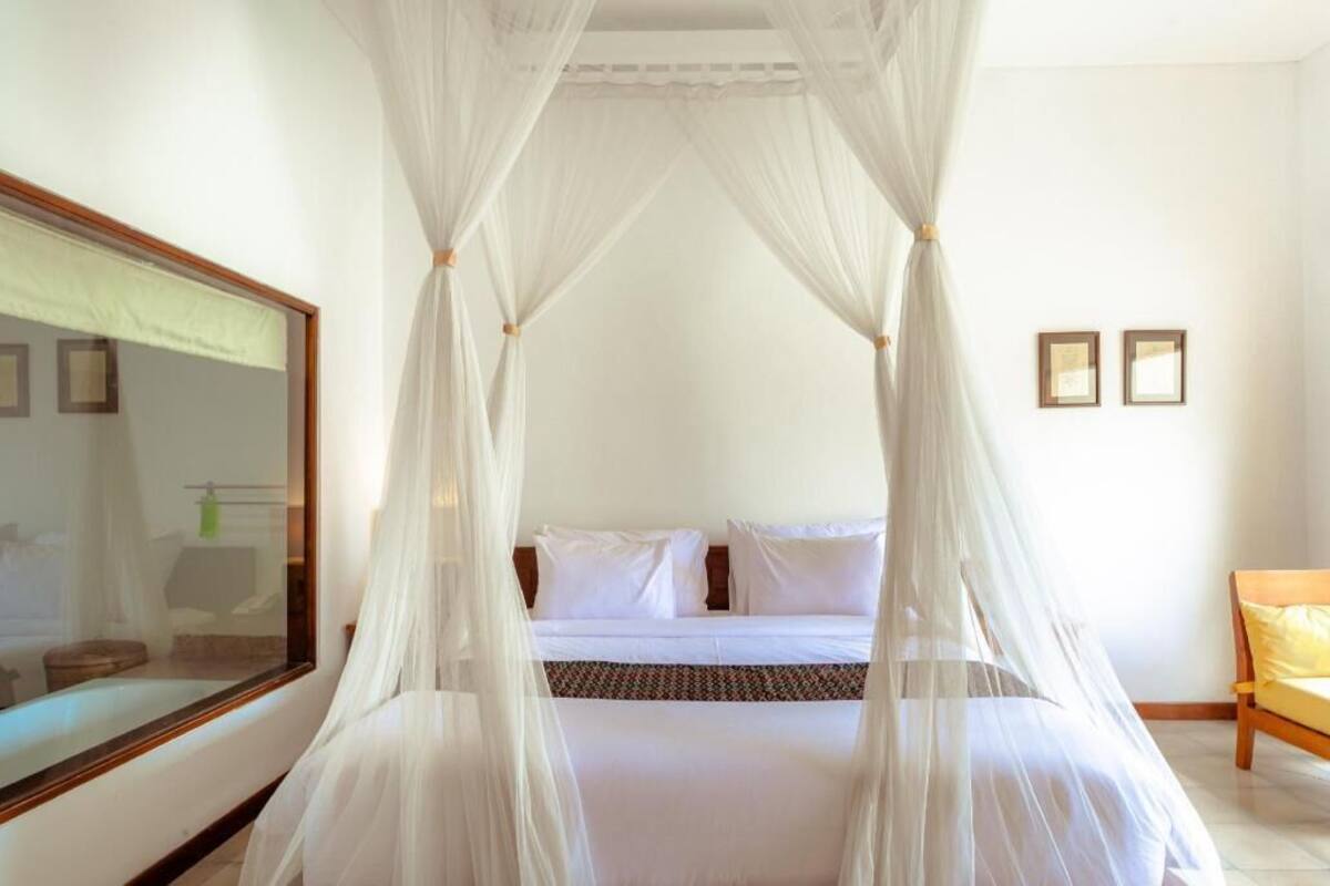 A bedroom with a four-poster canopy bed, a large mirror, and a wooden chair.