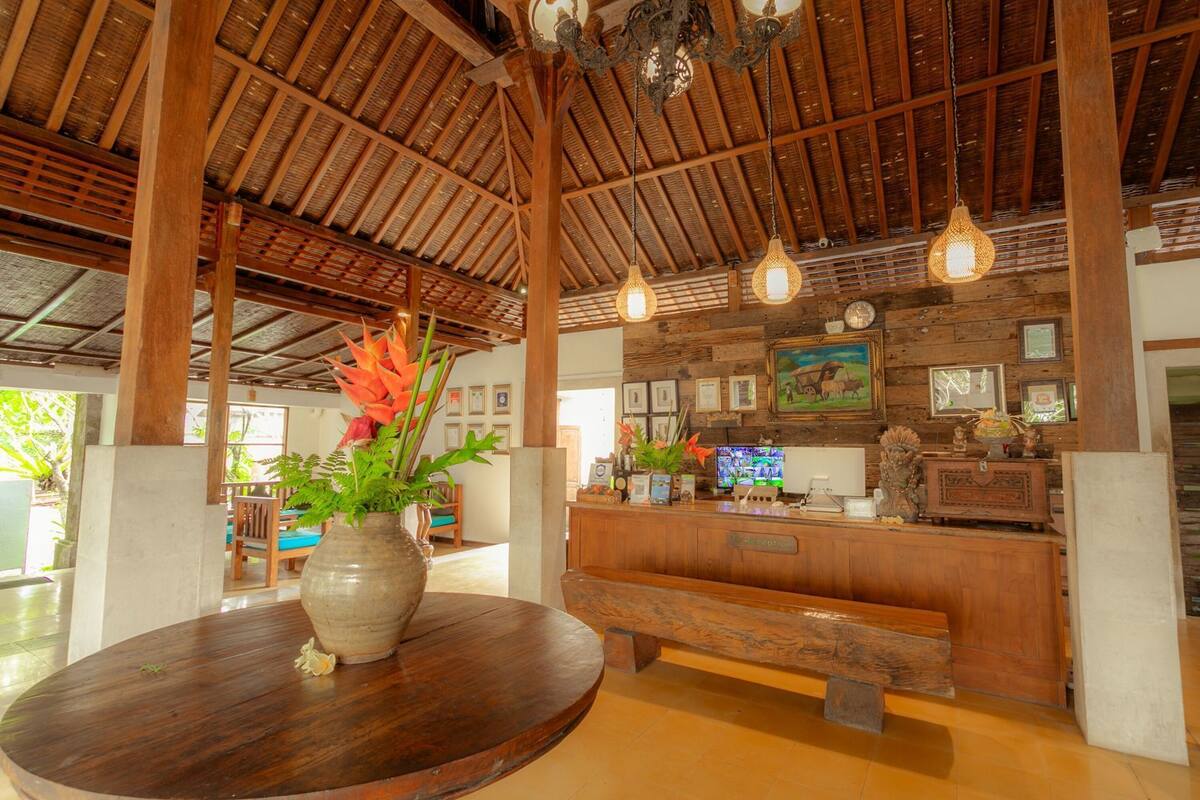 A reception area with a wooden reception desk, a bench, a vase with flowers, and a ceiling with wooden beams and hanging lights.