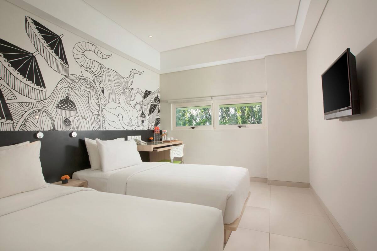 A modern hotel room with two beds, a large wall mural, a TV, and a window with a view of trees.